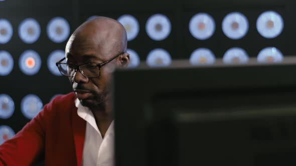Bearded serious african-american businessman is using computer in dark room.