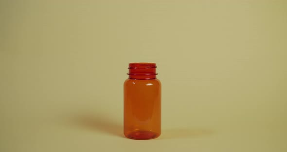 Slow motion wide shot of a single pill falling vertically towards a pill bottle, hitting the rim and alt