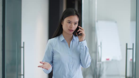 Young Professional Asian Woman Manager Talking to Client or Partner Via Cellphone Standing at Modern
