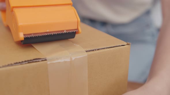 Close up shot of Young Asian Woman Hand Packing, Taping a Cardboard Box