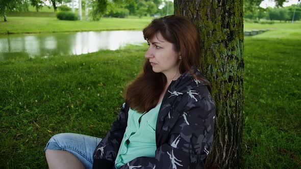 Sad Brunette Woman Sitting in the Park Near a Tree and Thinking About Something Memories