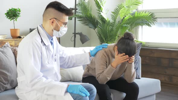 A Young Doctor Wearing Glasses and a Mask in a White Lab Coat Sits on a Sofa at a Meeting alt