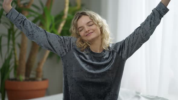 Medium Shot of Joyful Slim Smiling Woman Stretching in Bedroom at Home in the Morning alt