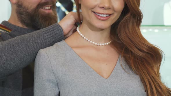 Cropped Shot of a Man Adjusting Pearl Necklace on the Neck of His Wife alt