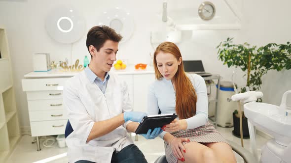Young Male Dentist and Female Patient Looking at Digital Tablet Discussing Dental Treatment Plan alt