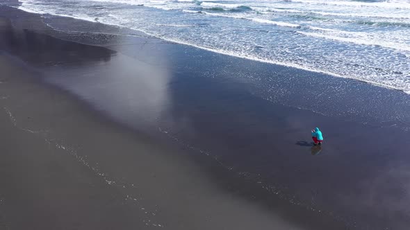 Aerial View of a Female Traveler Photographing Atlantic Ocean Waves on the Beach. Hofn, Iceland alt
