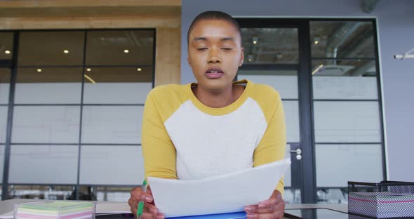 African american creative businesswoman at desk, reading, making notes and talking during video call alt