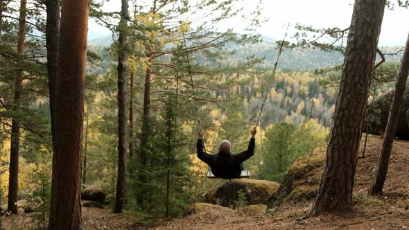A Young Happy Man Swings in the Forest with a Beautiful View of the Autumn Landscape in a Mountain