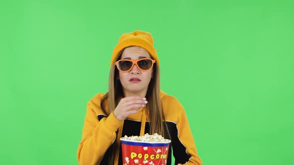 Portrait of Modern Girl in Yellow Hat in 3D Glasses Is Watching a Scary Movie and Eating Popcorn alt