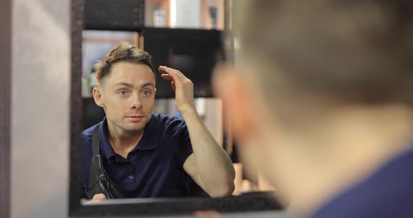 Man Straightens His Hair Looking in the Mirror in a Barbershop