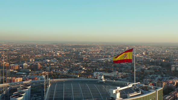 Fly Around Spanish Flag Waving in Wind on Rooftop of Business Skyscraper alt