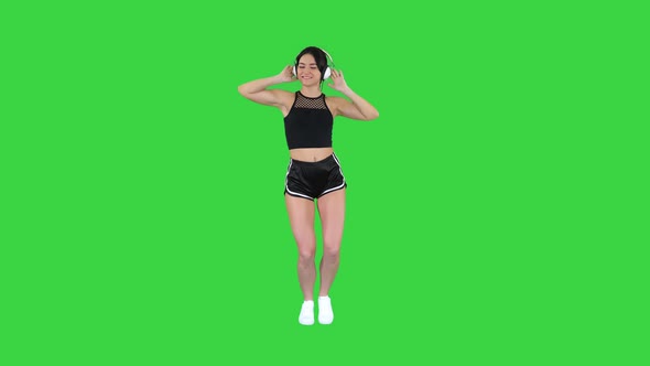 Young Happy Sportive Woman Listening Music in Headphones and Dancing on a Green Screen, Chroma Key. alt