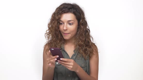 Portrait of Young Caucasian Woman with Brown Curly Hair Using Mobile Phone Reading Pleasant Text alt