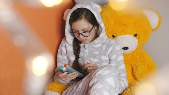 Girl in Pajamas Eating Tangerines and Use a Smartphone Lying on Bed