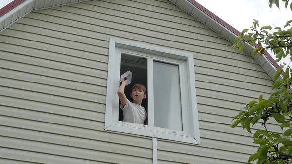 Young Boy Throws a Paper Plane Out of Window