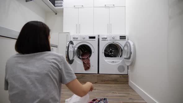Young Woman Having Fun Throwing Clothes Into Washing Machine in Laundry Room Slow Motion