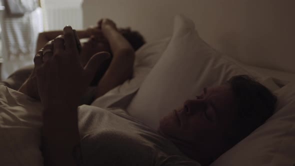 Mixed Race Couple waking up in bed looking at alarm on smart phone