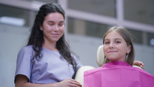 Portrait of Cute Teenage Girl in Dentist Chair Looking at Camera Smiling Gesturing Thumb Up with alt