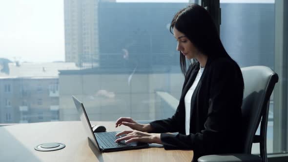Business Young Woman in Modern Office Skyscraper at Work at the Table at the Laptop