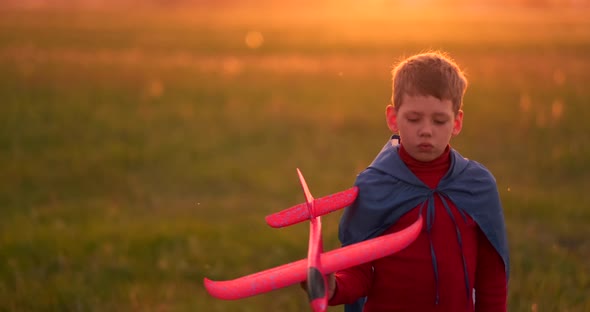 The Boy Runs Across the Field with a Plane in His Hands at Sunset alt