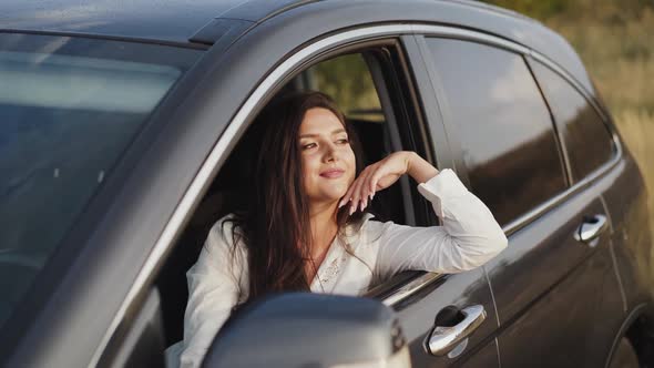 Pretty Girl Leans Out Car Window Looks Outside and Smiles alt
