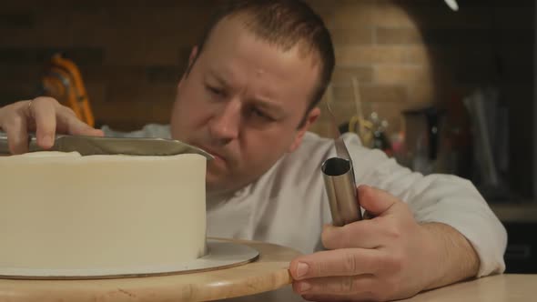 A Caucasian Male Pastry Chef Sits on His Knees and Aligns the Perfect Cake Blank