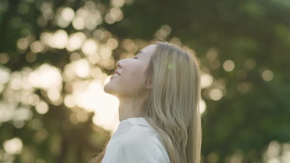 Asian female closed her eyes enjoying the breeze meadow in the public park during sunset.