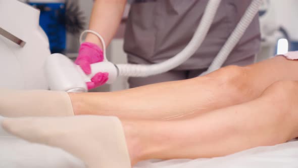Attractive Beautician Doing Laser Hair Removal on Legs of Beautiful Young Woman alt