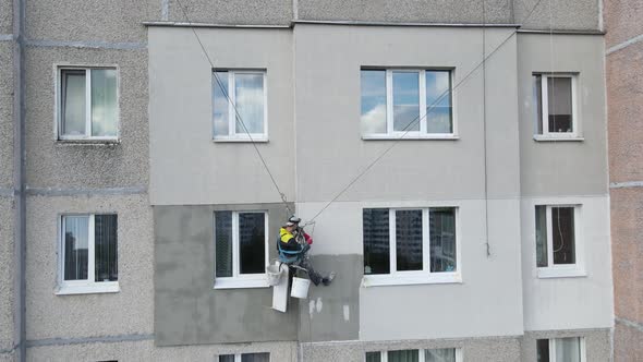 An Industrial Climber Suspended on Ropes and Paints the Wall of a Building with a Roller