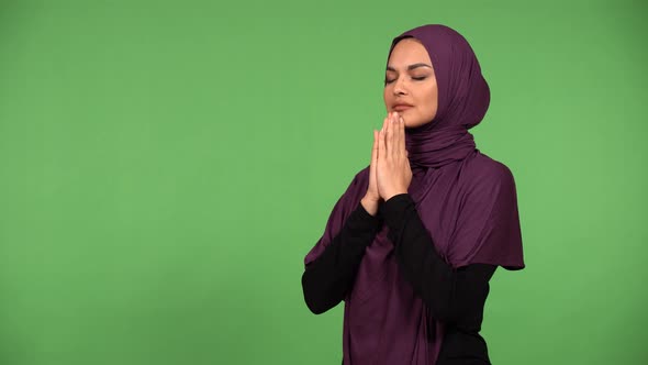 A Young Beautiful Muslim Woman Prays with Her Hands Clasped Together  Green Screen Background