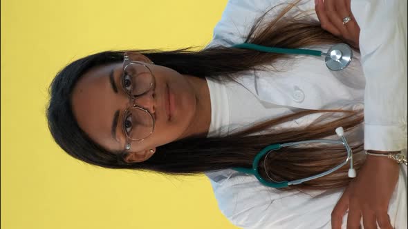 Close-up of Mixed-race Female Doctor Spreading Hands To the Sides on Yellow Background. alt