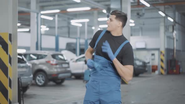 Positive Handsome Young Auto Mechanic in Uniform Dancing in Slow Motion in Repair Shop alt