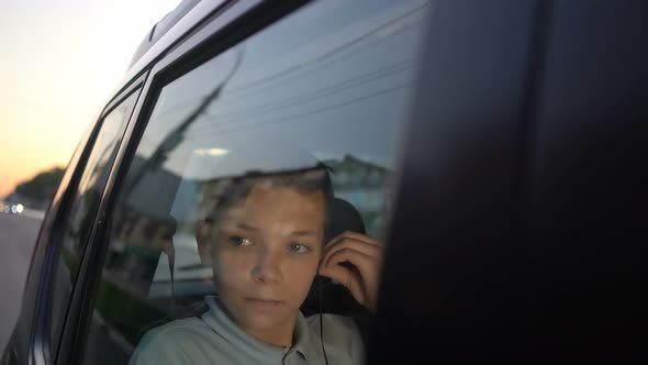 Teenager Boy with Headphones Listening To the Music in Backseat of Car and Looking Away alt