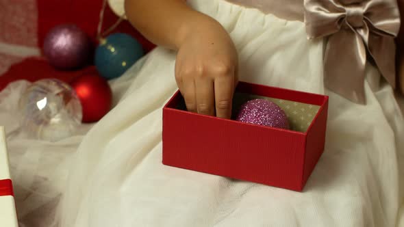A little girl in a beautiful outfit opens a gift for Christmas and New Year, Birthday alt