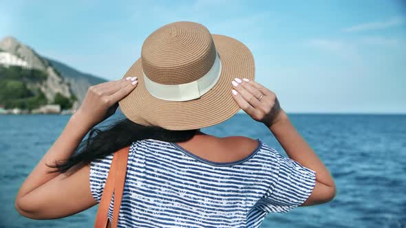 Back View Elegant Travel Woman in Straw Hat Admiring Seascape alt