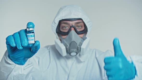 Virologist in a Protective Suit Shows a Developed COVID-19 Vaccine and Thumb Up. Concept of Global alt