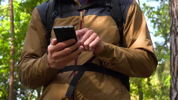 A Backpacker Works on a Smartphone in a Forest - Closeup alt