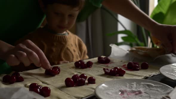Mother with a son cooking cookies with a cherry at home.