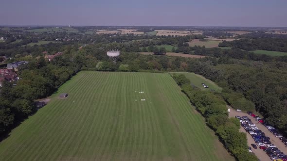 Drone aerial view flying over freshly cut field in Trent Park with car park and water tower in view. alt