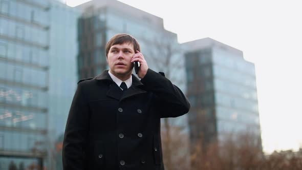A Businessman on the Street in a Black Coat is Talking on the Phone
