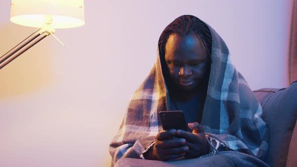 Sick African American Black Man Covered with Blanket Over the Head Using Smartphone alt