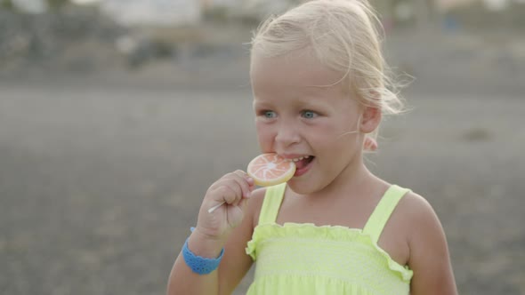 Funny three years old girl with a lollipop on the beach alt