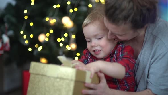 Little Toddler Boy with Mom Excitingly Looking Inside of Christmas Gift Box alt
