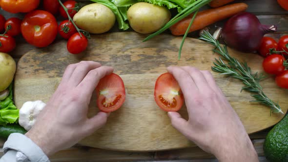 Male Hands Sliding Apart Two Halves of Tomato on Wooden Board alt