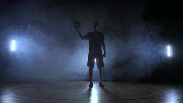 The Silhouette of a Basketball Player on a Dark Background with Smoke on the Basketball Court Throws alt