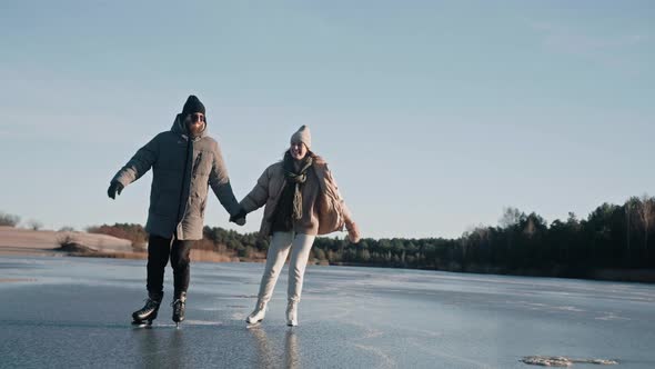 Couple is Skating on a Clear Frozen Lake on a Sunny Day with Beautiful Landscape