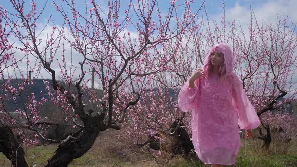 Woman in a Pink Hooded Dress with Flowers Walks Through a Peach Field alt