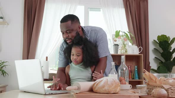 Happy moment. Black father helping daughter to use laptop at the home kitchen table