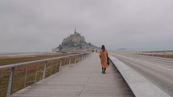 Camera Follows Elegant Woman Walking To Epic Amazing Mont Saint Michel Fortress Island on Grey