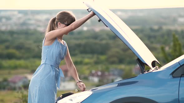 Young Female Driver Standing Alone Near a Broken Car with Popped Up Hood Inspecting Her Vehicle alt